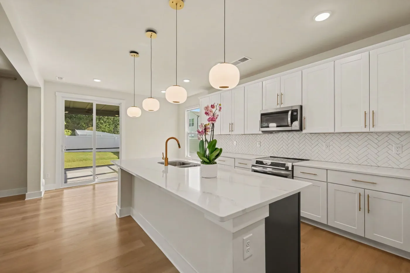 Kitchen with a large quartz island, gold pendant lights, and herringbone tile backsplash