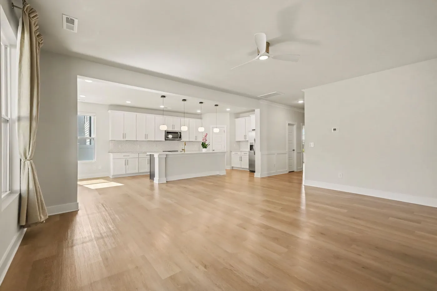 Open living room with light wood-look flooring flowing into the kitchen and island