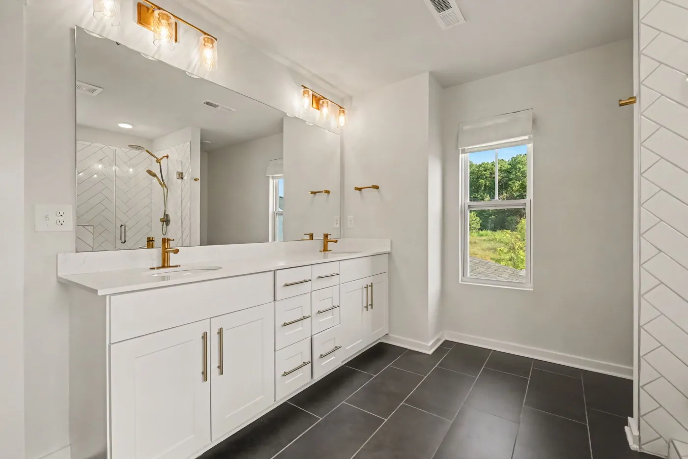 Primary bath with a double vanity, gold fixtures, and dark tile floor